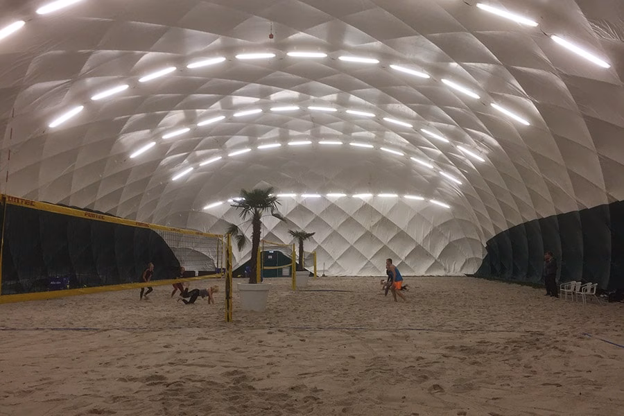 Paranet Nutzungskonzept Beachvolleyball 1 Indoor-Beachvolleyballfeld mit Palmen unter der beleuchteten Kuppel einer großen PARANET Traglufthalle.