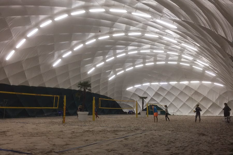 Paranet Nutzungskonzept Beachvolleyball 2 Menschen beim Beachvolleyball auf Sandplätzen im Innenraum einer beleuchteten Traglufthalle.