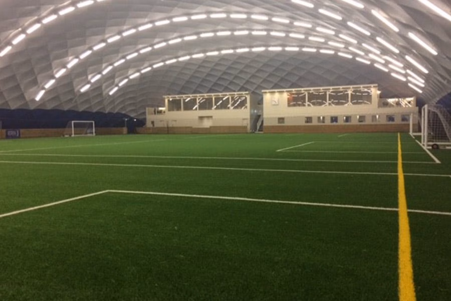 Paranet Nutzungskonzept Fußball Traglufthalle 3 Großes Kunstrasenfeld mit verglastem Anbau im Innenbereich einer beleuchteten Traglufthalle.