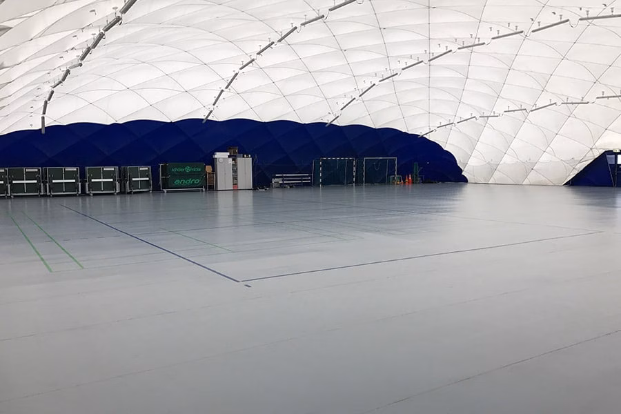 Paranet Nutzungskonzept Fußball Traglufthalle 4 Helle Sporthalle mit grauem Boden und blauen Randbereichen im Inneren einer Traglufthalle.