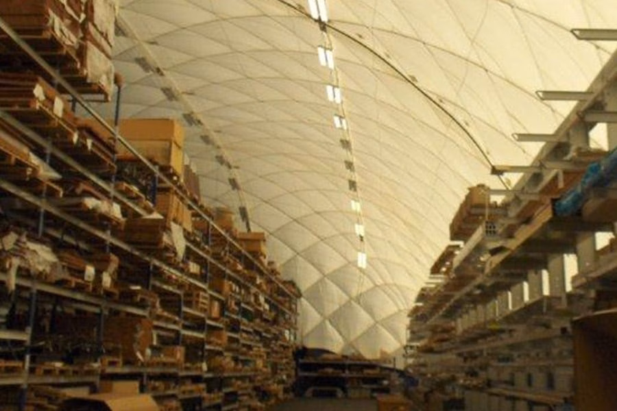 paranet-nutzungskonzept-logistik-galerie-1 Lagerhalle mit hoch gefüllten Regalen und Holzpaletten unter einer gewölbten Traglufthalle.