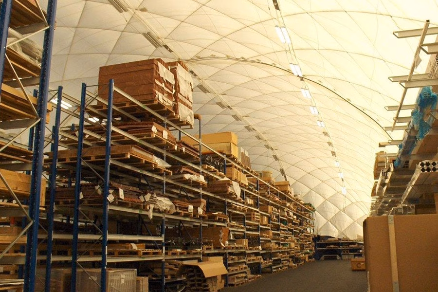 paranet-nutzungskonzept-logistik-galerie-2 Lagerhalle mit hoch gefüllten Regalen und Holzpaletten unter einer gewölbten Traglufthalle.