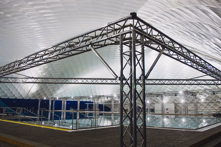 Paranet Nutzungskonzept Schwimmen 2 Blick durch eine metallene Licht-Traverse auf ein Schwimmbecken unter einer Traglufthalle.