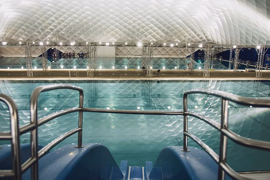 Paranet Nutzungskonzept Schwimmen 8 Blick von einer blauen Wasserrutsche auf das Schwimmbecken in einer hellen Traglufthalle.