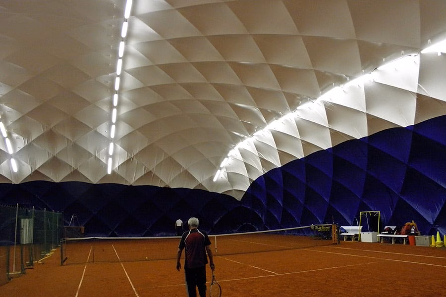 Paranet Nutzungskonzept Tennis Traglufthalle 4 Ein Tennisspieler von hinten auf einem Rotsandplatz in einer Traglufthalle mit blauen Wänden.