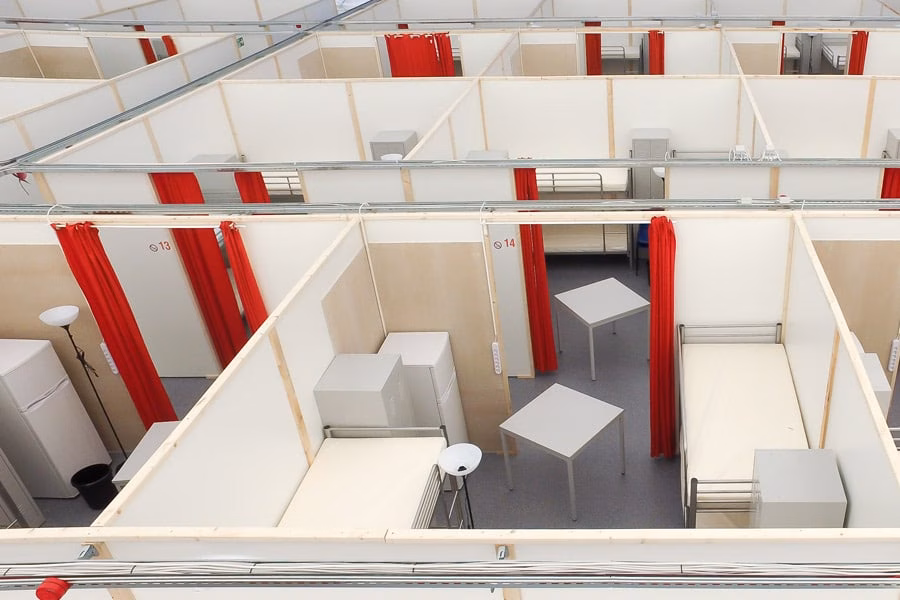 Paranet Nutzungskonzept Caredome 2 Blick von oben auf abgetrennte Wohnkabinen mit Betten, Tischen und roten Vorhängen in einer Notunterkunft.