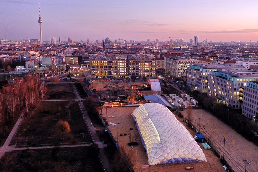 Paranet Traglufthalle Galerie 5 Luftaufnahme bei Dämmerung mit einer beleuchteten Traglufthalle und dem Berliner Fernsehturm am Horizont.