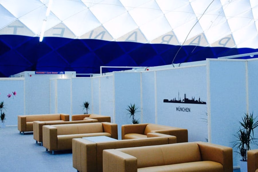 Loungebereich mit braunen Ledersofas vor weißer Wand mit München-Skyline unter einer Traglufthalle.