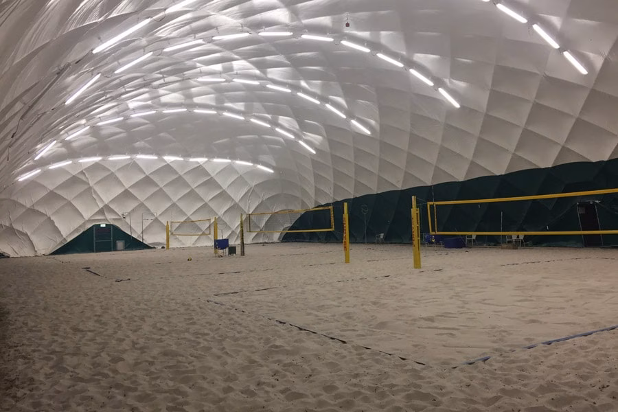 Indoor-Beachvolleyballfelder auf Sand unter der beleuchteten Kuppel einer Traglufthalle.