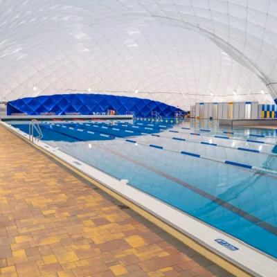 Großes Hallenbad mit mehreren Schwimmbahnen und blauer Auskleidung unter einer Traghalle.