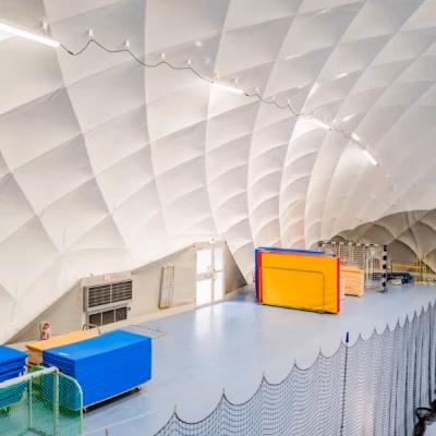Sporthalle mit blauem Boden, Stapeln von Turnmatten und Toren unter einer Traghalle.